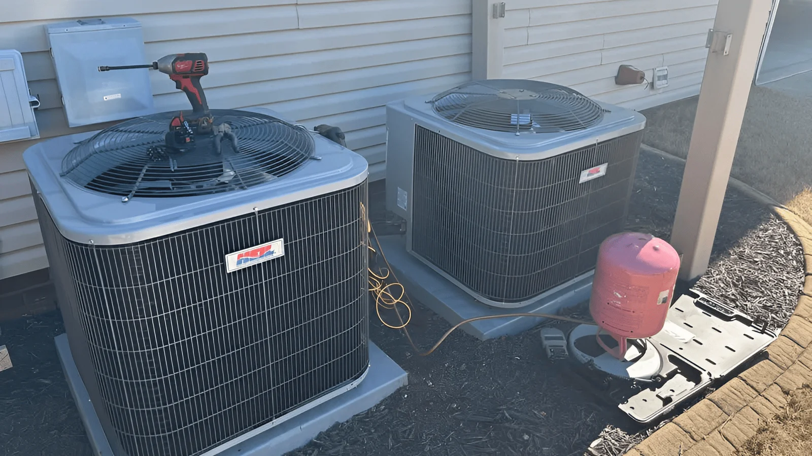 Two AC condenser units installed on concrete pad with refrigerant lines and electrical connections