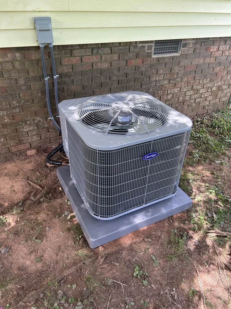 New Carrier AC condenser unit on concrete pad with refrigerant lines and disconnect switch